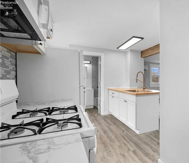 kitchen with sink, gas range gas stove, white cabinetry, light hardwood / wood-style flooring, and range hood