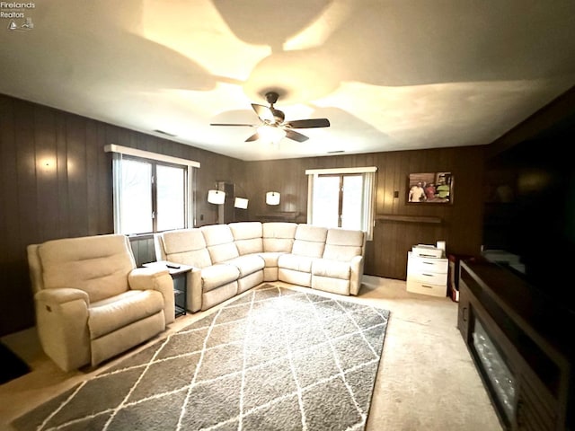 living room with ceiling fan, wooden walls, and light carpet