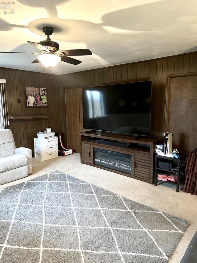 living room featuring ceiling fan, wooden walls, and carpet