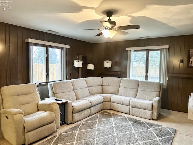 carpeted living room with ceiling fan and wood walls