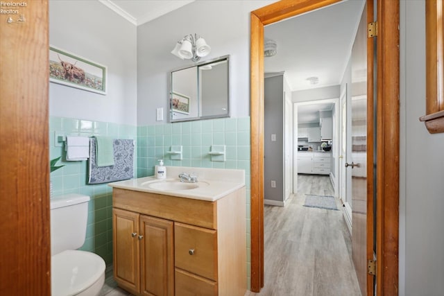 bathroom featuring toilet, wood-type flooring, tile walls, ornamental molding, and vanity