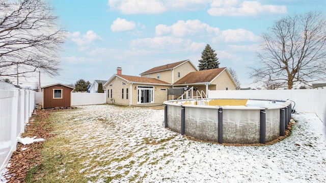 snow covered house featuring a storage shed and a fenced in pool