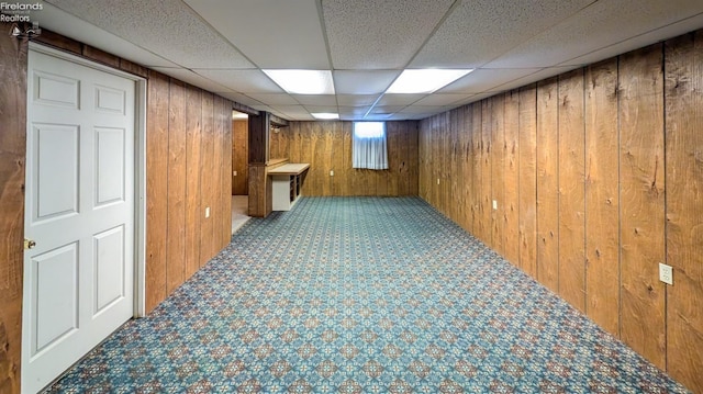 basement with carpet flooring, a drop ceiling, and wooden walls