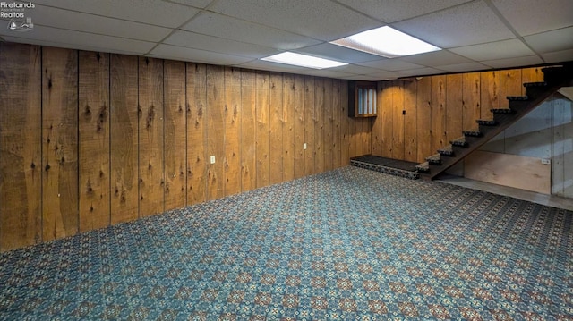 basement featuring a drop ceiling, carpet, and wood walls