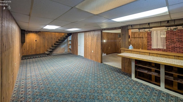 basement featuring carpet flooring, a paneled ceiling, and wood walls