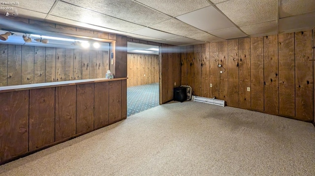 basement featuring a baseboard radiator, light colored carpet, a drop ceiling, and wood walls