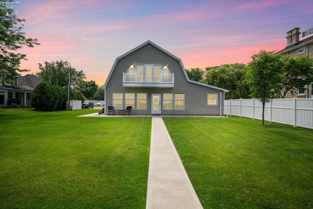 back house at dusk featuring a patio, a balcony, and a yard