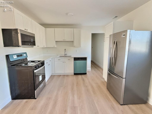 kitchen with appliances with stainless steel finishes, sink, white cabinets, and light hardwood / wood-style flooring