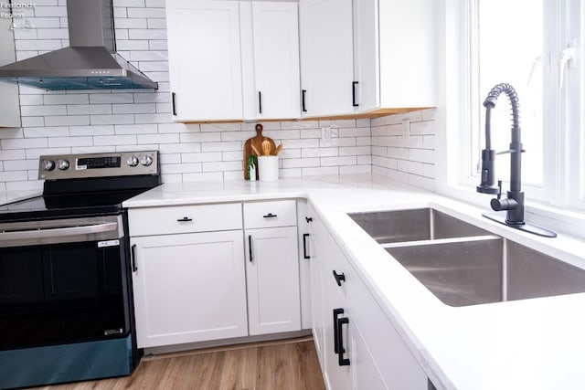 kitchen featuring stainless steel electric stove, white cabinetry, sink, decorative backsplash, and wall chimney range hood