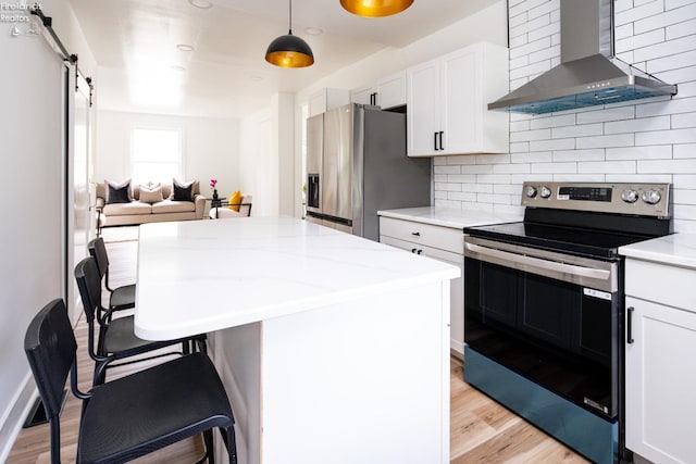 kitchen featuring white cabinetry, wall chimney exhaust hood, stainless steel appliances, and a barn door