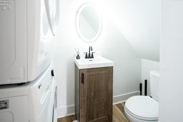 bathroom featuring vanity, wood-type flooring, stacked washer / drying machine, and toilet