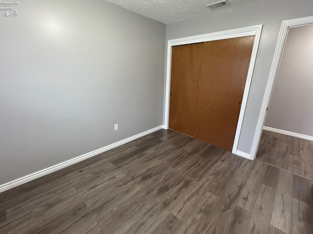 unfurnished bedroom with dark hardwood / wood-style floors, a textured ceiling, and a closet