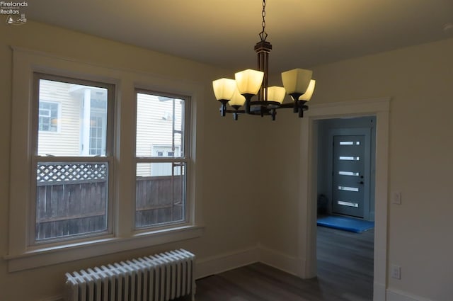 unfurnished dining area with dark hardwood / wood-style floors, radiator, and a notable chandelier