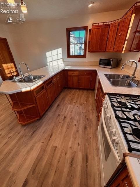 kitchen with white gas stove, kitchen peninsula, sink, and light hardwood / wood-style flooring