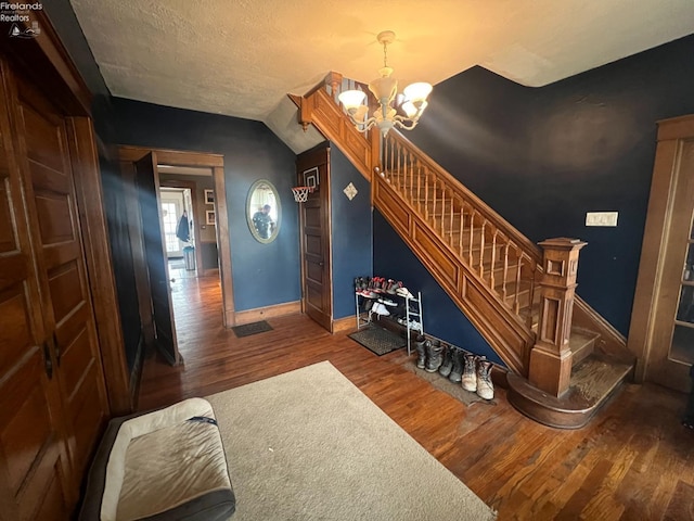 staircase with lofted ceiling, a notable chandelier, hardwood / wood-style flooring, and a textured ceiling