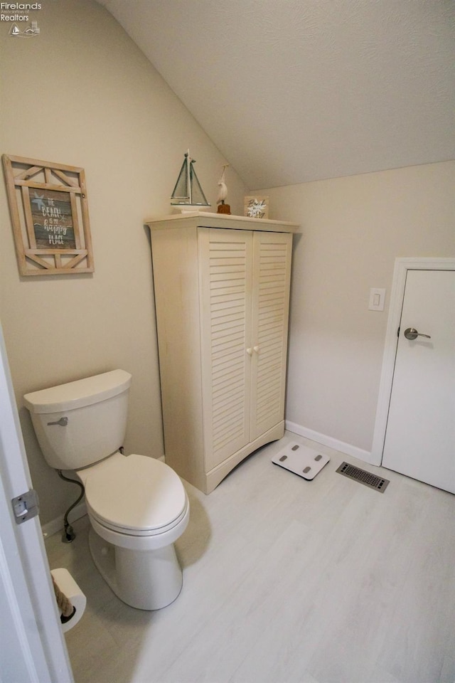 bathroom with wood-type flooring, toilet, and vaulted ceiling