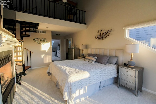 bedroom with light carpet, a tiled fireplace, and a towering ceiling