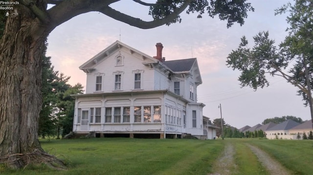 back house at dusk with a lawn and a sunroom