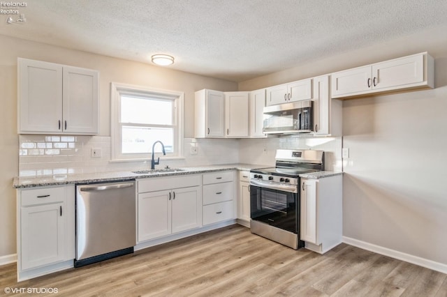 kitchen with stainless steel appliances, white cabinetry, sink, and light hardwood / wood-style floors