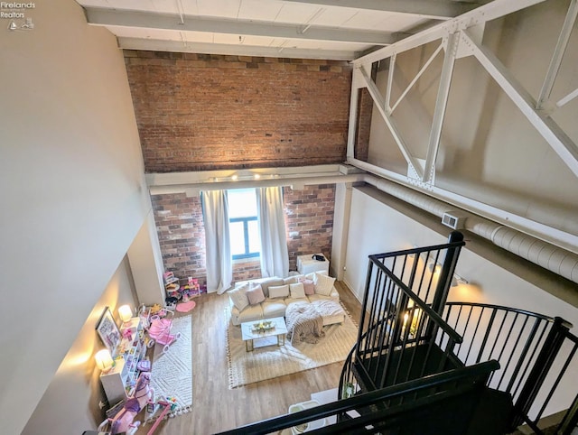 living room with beam ceiling, high vaulted ceiling, hardwood / wood-style flooring, and brick wall