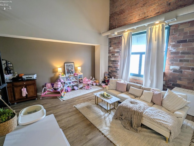 living room featuring brick wall, a towering ceiling, and hardwood / wood-style floors