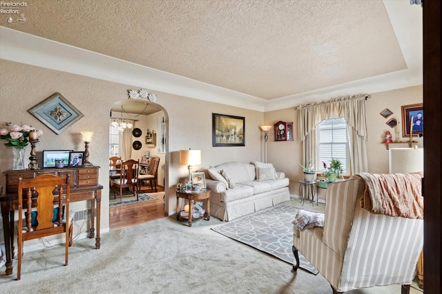 living room with an inviting chandelier, carpet floors, a raised ceiling, and a textured ceiling