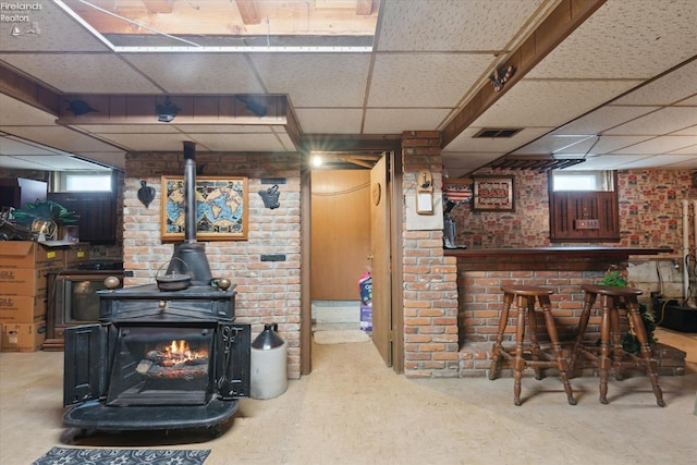 living room featuring bar, a drop ceiling, brick wall, and a wood stove