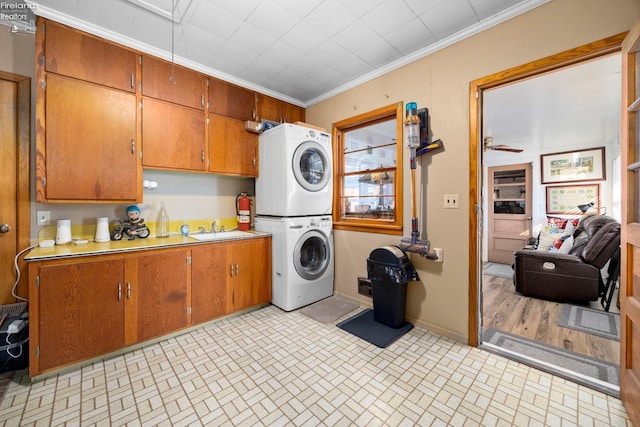 washroom with cabinets, stacked washing maching and dryer, ornamental molding, and sink