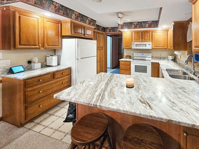 kitchen featuring sink, white appliances, a breakfast bar, ceiling fan, and kitchen peninsula