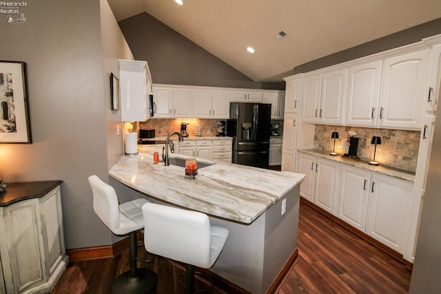 kitchen with dark hardwood / wood-style flooring, refrigerator with ice dispenser, light stone countertops, and white cabinets