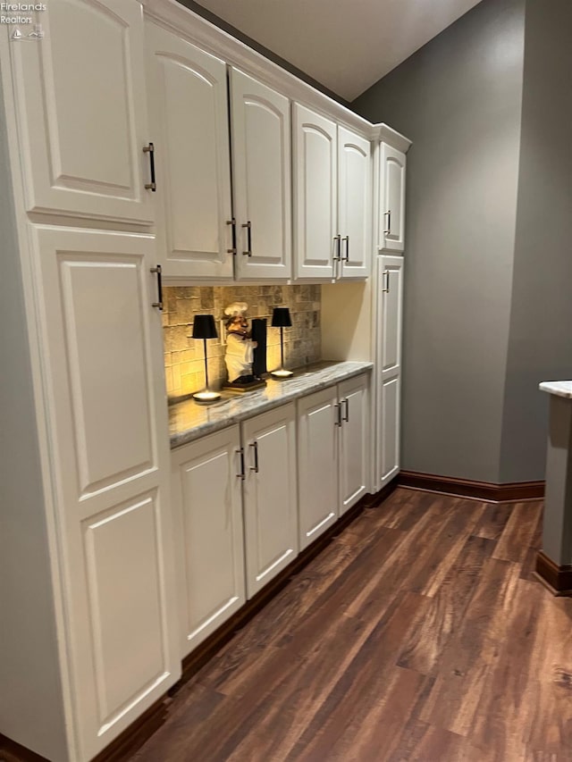 bar with tasteful backsplash, light stone counters, white cabinets, and dark hardwood / wood-style flooring