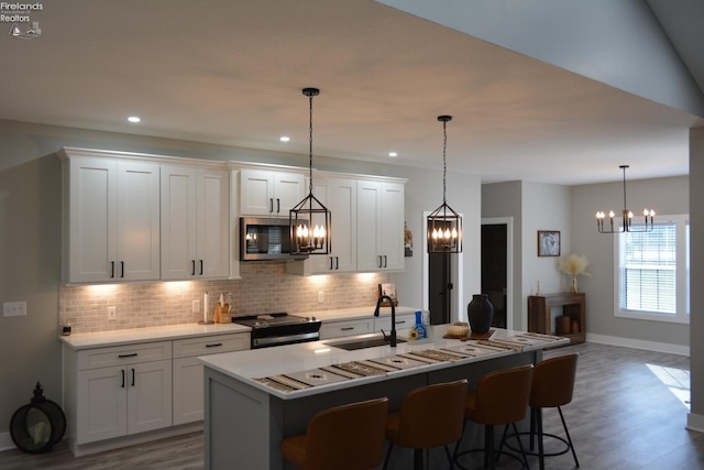 kitchen with an island with sink, pendant lighting, stainless steel appliances, decorative backsplash, and white cabinets