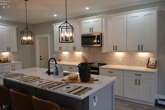 kitchen featuring hanging light fixtures, an island with sink, white cabinets, and black range with electric cooktop