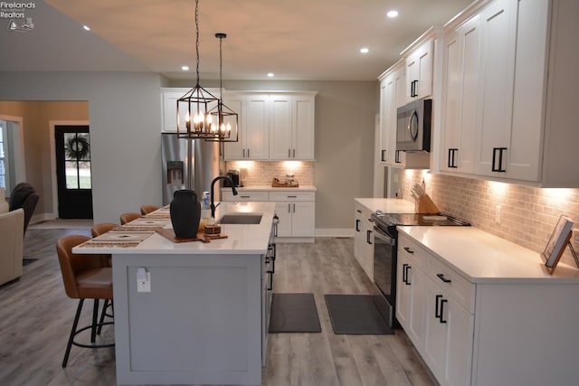 kitchen featuring sink, stainless steel refrigerator with ice dispenser, range with electric stovetop, an island with sink, and decorative light fixtures