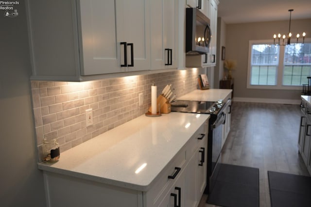 kitchen with pendant lighting, light stone counters, tasteful backsplash, black electric range, and white cabinets