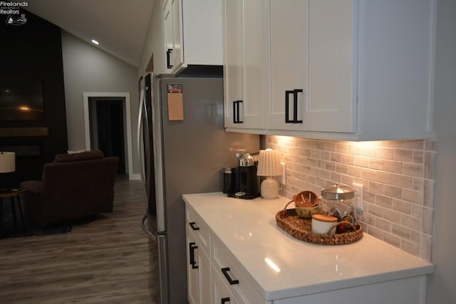 kitchen with tasteful backsplash, vaulted ceiling, white cabinets, and light stone counters