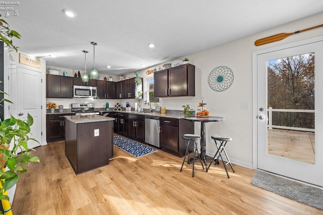 kitchen featuring a breakfast bar, stainless steel appliances, dark brown cabinetry, a kitchen island, and decorative light fixtures