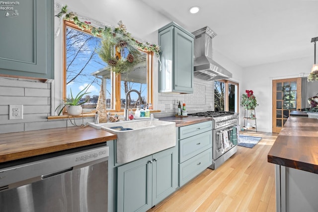 kitchen with sink, butcher block countertops, appliances with stainless steel finishes, range hood, and backsplash