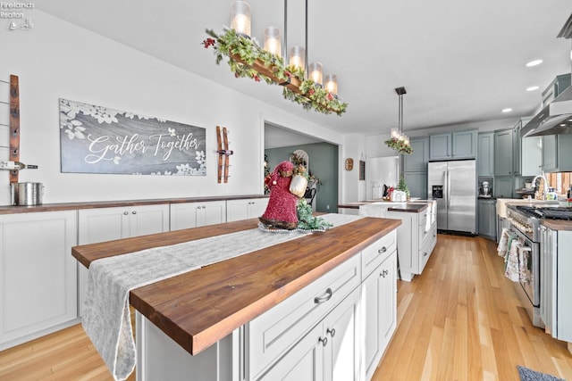 kitchen featuring wooden counters, decorative light fixtures, a center island, light wood-type flooring, and stainless steel appliances