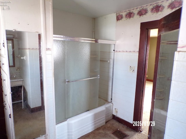 bathroom featuring tile walls and bath / shower combo with glass door