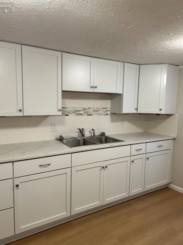 kitchen with white cabinetry, sink, light hardwood / wood-style flooring, and backsplash