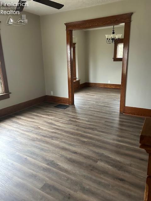 unfurnished room with dark hardwood / wood-style floors and ceiling fan with notable chandelier