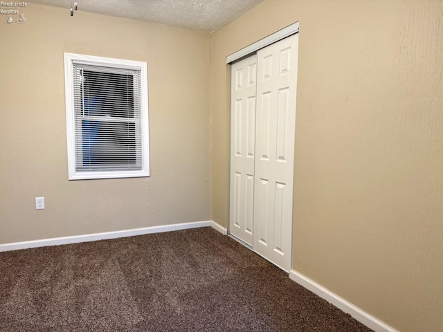 unfurnished bedroom with dark colored carpet, a textured ceiling, and a closet