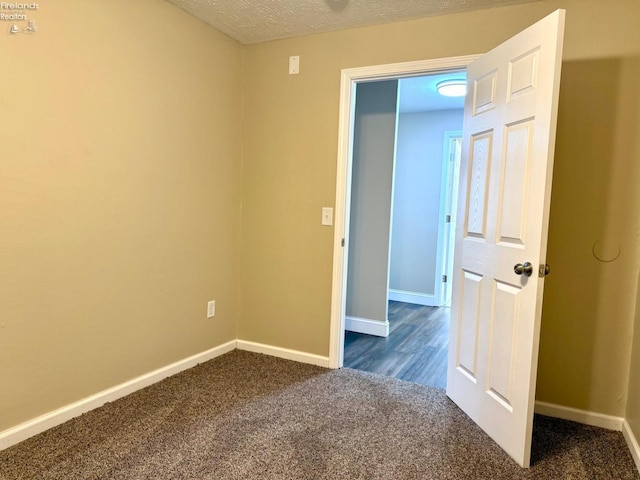 spare room featuring a textured ceiling and dark carpet