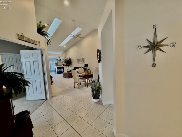 hallway featuring high vaulted ceiling, a skylight, and light colored carpet