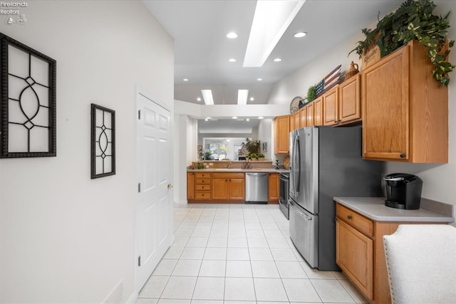 kitchen with stainless steel appliances, lofted ceiling with skylight, and light tile patterned floors