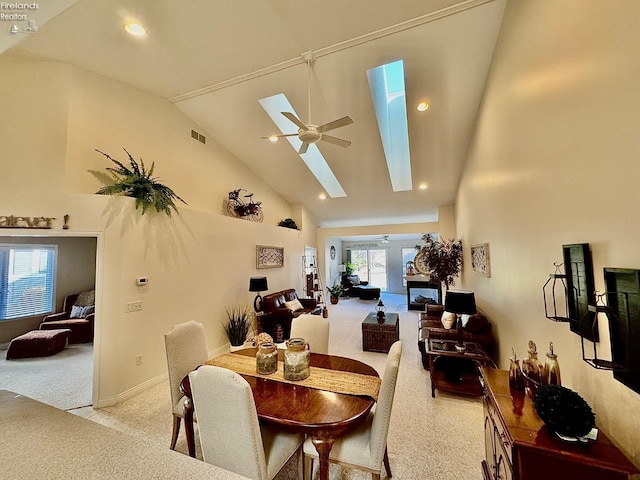 carpeted dining area with ceiling fan, a skylight, and high vaulted ceiling