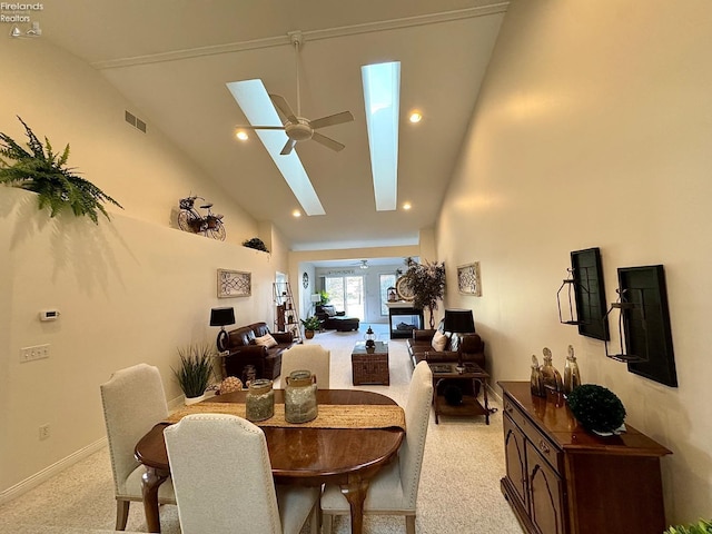 dining space with light colored carpet, ceiling fan, a skylight, and high vaulted ceiling