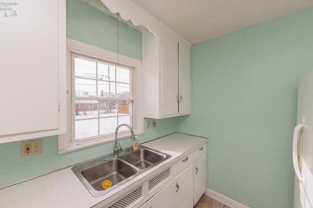 kitchen featuring sink, white cabinetry, and fridge