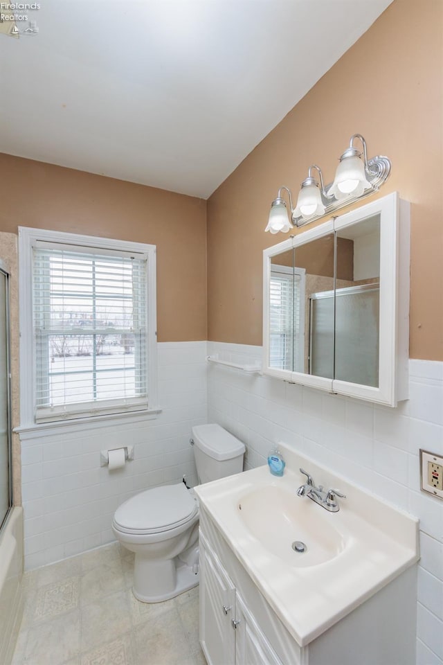 full bathroom with tile walls, toilet, vanity, and combined bath / shower with glass door